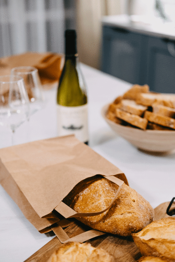 Bolsa de asa de papel kraft con una barra de pan metid al lado de una botella de vino