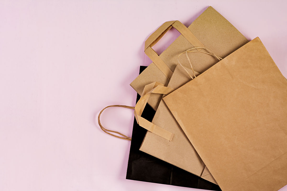Bolsas de papel kraft con asa amontonadas sobre un fondo rosa