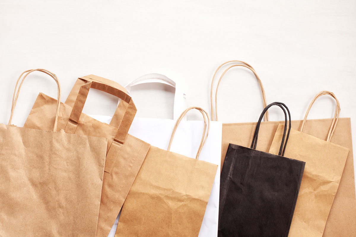 Bolsas de papel kraft de diferentes colores amontonadas sobre un fondo crema